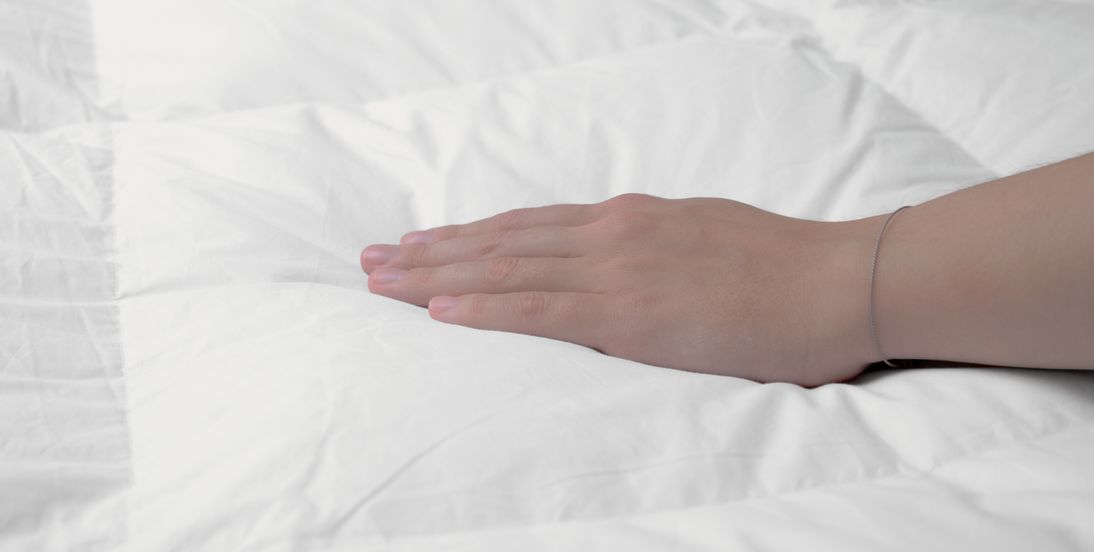 Eine Hand liegt sanft auf einer weißen, gesteppten Daunendecke.